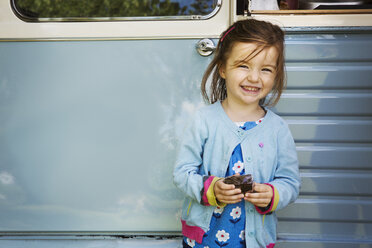 Ein lächelndes Mädchen steht vor einem blauen mobilen Café und hält einen Schokoladen-Brownie in der Hand. - MINF05610