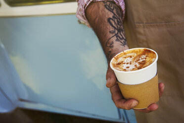 Close up of man with tattoo on his arm holding paper cup with cappuccino. - MINF05613