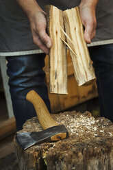 Nahaufnahme einer Person, die einen kleinen, in zwei Hälften gespaltenen Holzklotz und eine Handaxt hält, die auf einem Spaltblock liegt - MINF05614