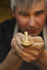 A craftsman holding and inspecting a handcrafted hand made wooden spoon with a long slender handle and round polished bowl. - MINF05617