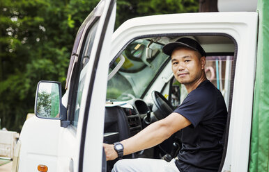 Ein junger Mann sitzt in einem Lastwagen auf einem landwirtschaftlichen Betrieb in Japan. - MINF05634