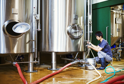 Mann bei der Arbeit in einer Brauerei, kniend neben einem metallenen Biertank. - MINF05638