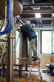 Mann, der in einer Brauerei arbeitet, um die Maschinen zu justieren und zu überprüfen, die das gebraute Bier durch die Verarbeitungsanlage transportieren. - MINF05639