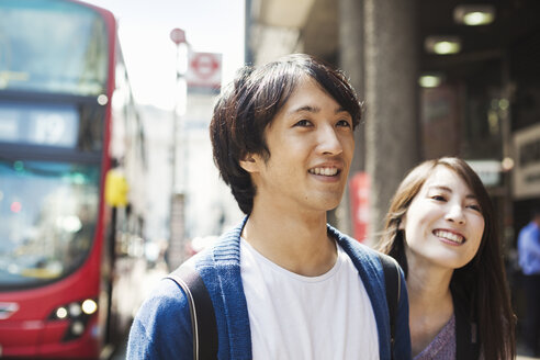 Eine junge japanische Frau und ein Mann, ein Paar auf der Straße in London, ein roter Bus im Hintergrund. - MINF05642