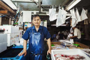 A traditional fresh fish market in Tokyo. A man in a blue apron standing behind the counter of his stall. - MINF05689