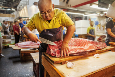 Ein traditioneller Frischfischmarkt in Tokio: Ein Fischhändler filetiert einen großen Fisch auf einer Platte, im Hintergrund Menschen. - MINF05691