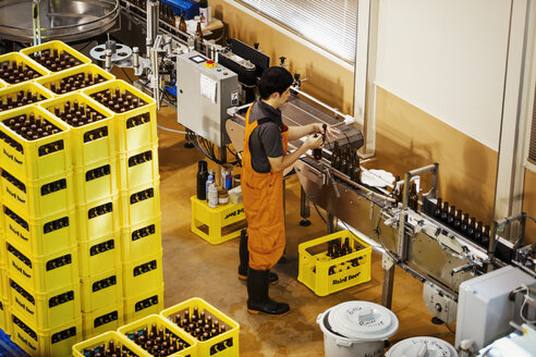 Arbeiter steht neben gelben Plastikkisten mit Bierflaschen in einer Brauerei. - MINF05701