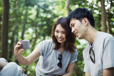 Junge Frau und ein Mann sitzen im Wald und machen ein Selfie. - MINF05714