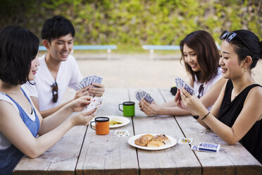 Drei junge Frauen und ein Mann sitzen an einem Tisch und spielen Karten. - MINF05719