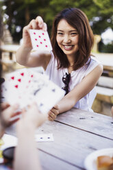 Lächelnde junge Frau, die an einem Tisch sitzt und Karten spielt. - MINF05720