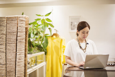 Frau in einer Modeboutique in Tokio, Japan, bei der Arbeit am Laptop. - MINF05727