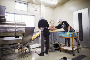 Arbeiter in Schürzen und Mützen nehmen frisch geschnittene Nudeln vom Förderband, um sie zu verpacken und zu verkaufen. - MINF05743