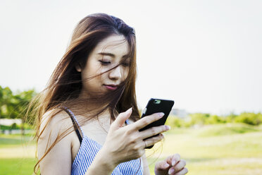 Lächelnde junge Frau mit langen braunen Haaren, die ein Mobiltelefon in der Hand hält. - MINF05758