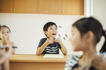 Drei Kinder, ein Junge und zwei Mädchen, in einem Klassenzimmer. - MINF05766