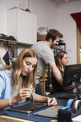 A man standing behind two women sitting working on circuitry in a technology lab. - MINF05772