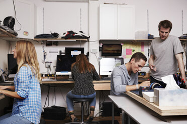 Two women and two men in a technology repair shop or lab, working on computers. - MINF05775