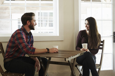 A young man and woman sitting at a table holding paper cups. - MINF05781