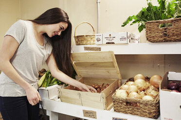 Eine Frau wählt in einem Hofladen Gemüse aus einer Auslage aus. - MINF05783