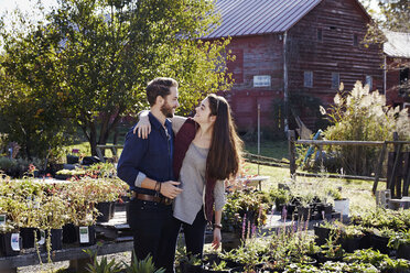 A young man and woman hugging among displays of plants at a garden centre. - MINF05789