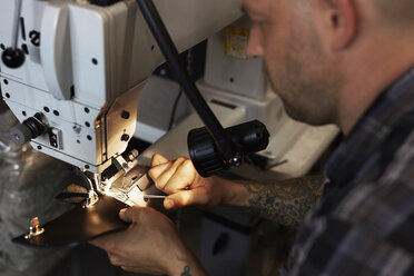 Ein Mann mit einer industriellen Nähmaschine, der handgefertigte Lederwaren näht. - MINF05800