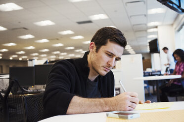 Ein Mann sitzt an einem Tisch in einem Büro und schreibt. - MINF05816