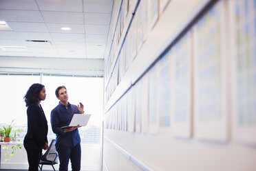 A woman and a man standing in an office looking at a laptop computer together, in front of a display on a wall. - MINF05826