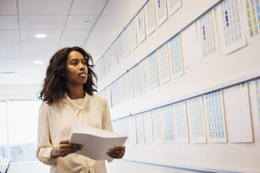 A woman standing in an office looking at a display holding pieces of paper. - MINF05830