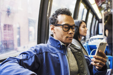 Ein junger Mann und eine junge Frau sitzen in einem öffentlichen Verkehrsmittel und schauen auf ihre Handys. - MINF05836