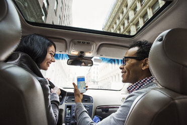 A young woman and young man in a car looking at a map on the display of a cell phone, seen from the back seat. - MINF05839