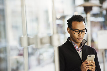 A young man holding at a cell phone and smiling. - MINF05840