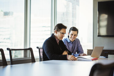 Two men at a table in a meeting room looking at a laptop computer. - MINF05846