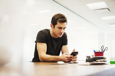 A young man sitting in a classroom leaning on a desk looking down at a cell phone. - MINF05858