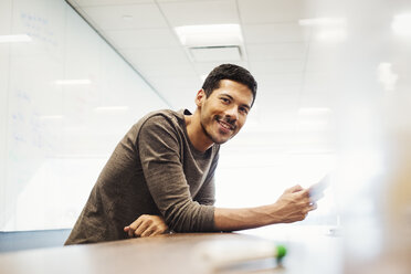 A young man sitting in a classroom leaning on a desk and smiling. - MINF05859