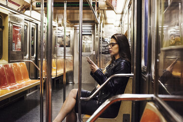 A woman sitting in a metro subway carriage looking at her cell phone. - MINF05867