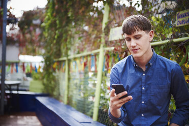 Ein junger Mann sitzt im Freien und schaut auf sein Handy. - MINF05870