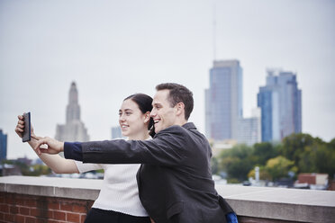 A young woman and a young man standing on a rooftop looking at a cell phone together. - MINF05880