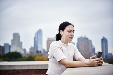 A young woman standing on a rooftop looking at a cell phone. - MINF05881