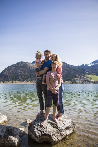 Österreich, Tirol, Walchsee, glückliche Familie auf Felsbrocken im See stehend, lizenzfreies Stockfoto