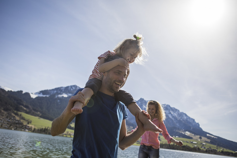 Österreich, Tirol, Walchsee, glücklicher Vater trägt Tochter auf den Schultern am See, lizenzfreies Stockfoto