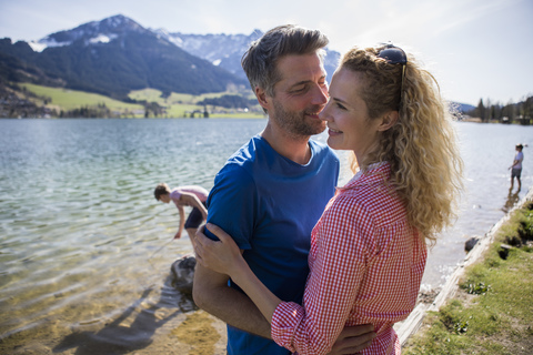 Austria, Tyrol, Walchsee, happy couple embracing at the lake with family in background stock photo