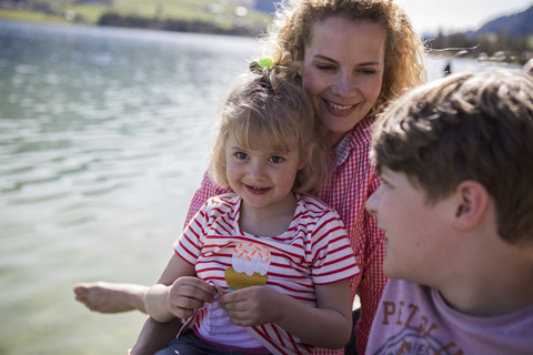 Österreich, Tirol, Walchsee, glückliche Mutter mit zwei Kindern am Seeufer, lizenzfreies Stockfoto