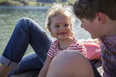 Austria, Tyrol, Walchsee, happy brother and sister smiling at each other at the lakeside - JLOF00164