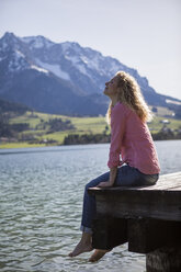 Austria, Tyrol, Walchsee, smiling woman sitting on a jetty at the lake - JLOF00184