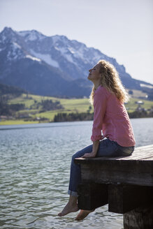 Österreich, Tirol, Walchsee, lächelnde Frau sitzt auf einem Steg am See - JLOF00184