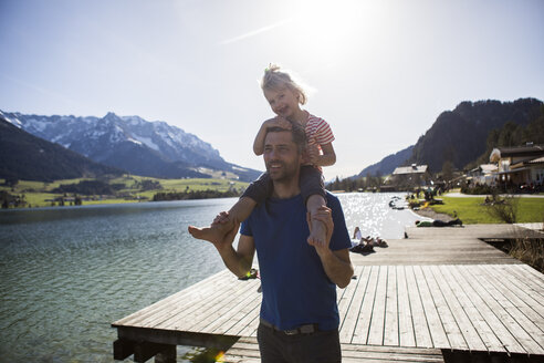 Austria, Tyrol, Walchsee, happy father carrying daughter on shoulders at the lake - JLOF00185