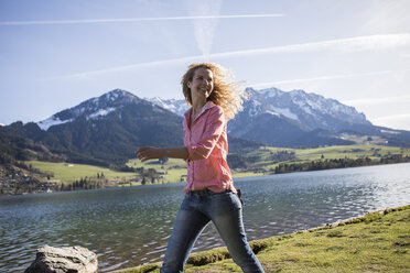 Austria, Tyrol, Walchsee, smiling woman walking at the lake - JLOF00194
