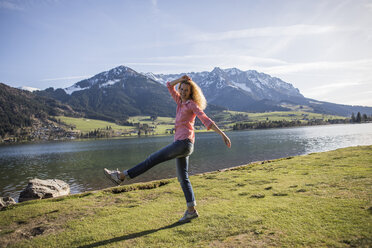 Austria, Tyrol, Walchsee, happy woman striding at the lake - JLOF00198