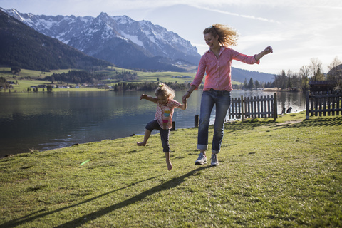 Austria, Tyrol, Walchsee, carefree mother and daughter jumping at the lake stock photo