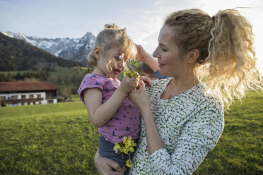 Österreich, Tirol, Walchsee, Mutter trägt Tochter mit Blumen auf einer Almwiese - JLOF00210