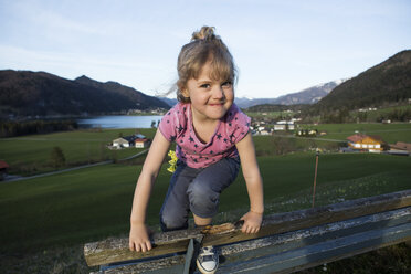 Österreich, Tirol, Walchsee, glückliches Mädchen auf einer Bank - JLOF00211